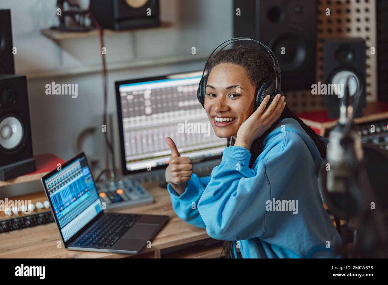 Anchorwoman, bella donna africana mostra pollice in su guardando la telecamera mentre trasmette in radio in studio di registrazione del suono Foto Stock