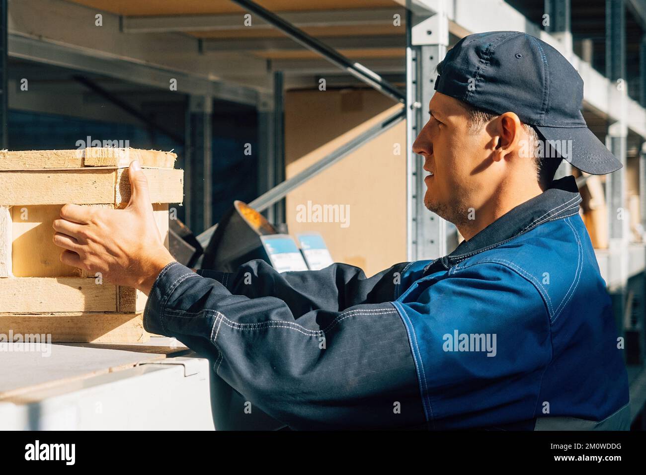 Il depositario dispone le scatole sui rack del magazzino. Operaio caucasico al lavoro in magazzino di cernita. Ritratto autentico sul lato. Foto Stock