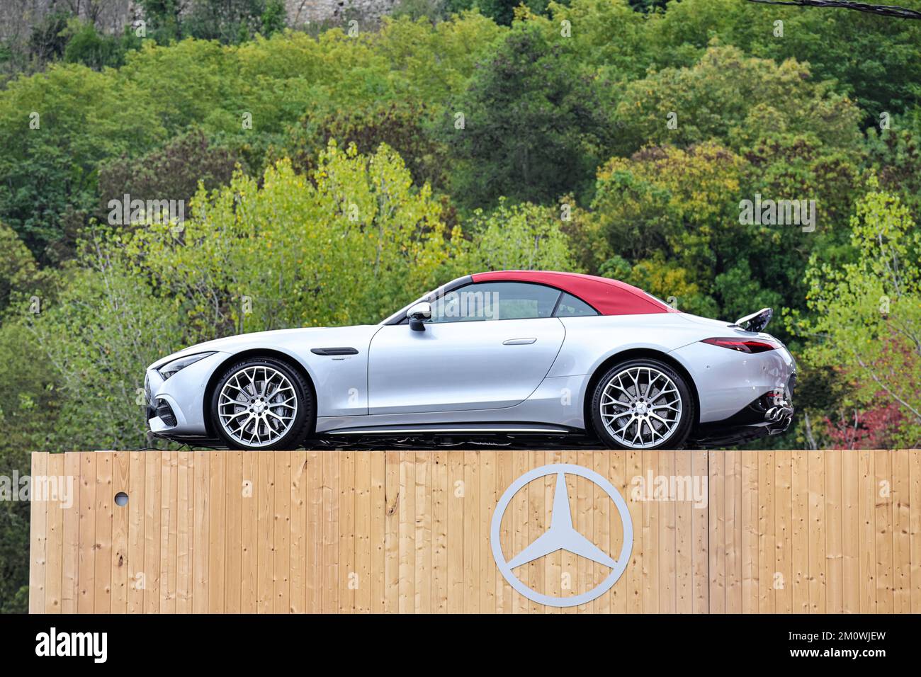 Una vettura sportiva Mercedes modello SL 43 grigio-argento, esposta all'esterno dell'azienda su un piedistallo in legno con il logo Mercedes Foto Stock