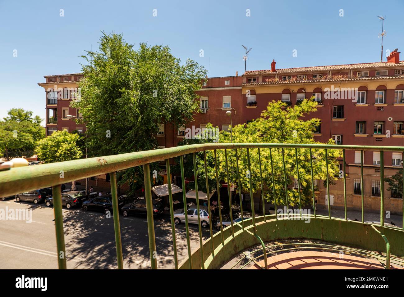 Vista su un edificio con alberi frondosi sulla facciata da una terrazza con una ringhiera di metallo verde Foto Stock