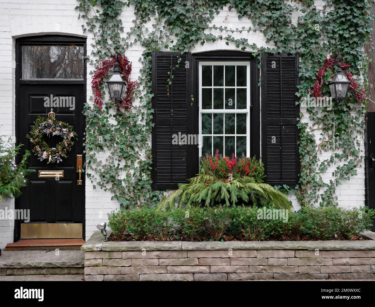 Davanti alla vecchia casa in mattoni con corona di Natale sulla porta d'ingresso e decorazioni a bacche sacre Foto Stock