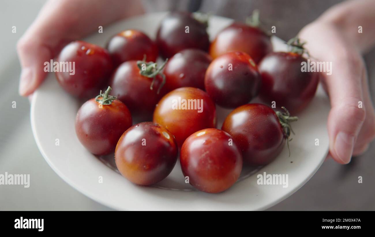 Commercio al dettaglio e commercio, pomodori neri maturi su un piatto nelle mani di una donna. Foto Stock