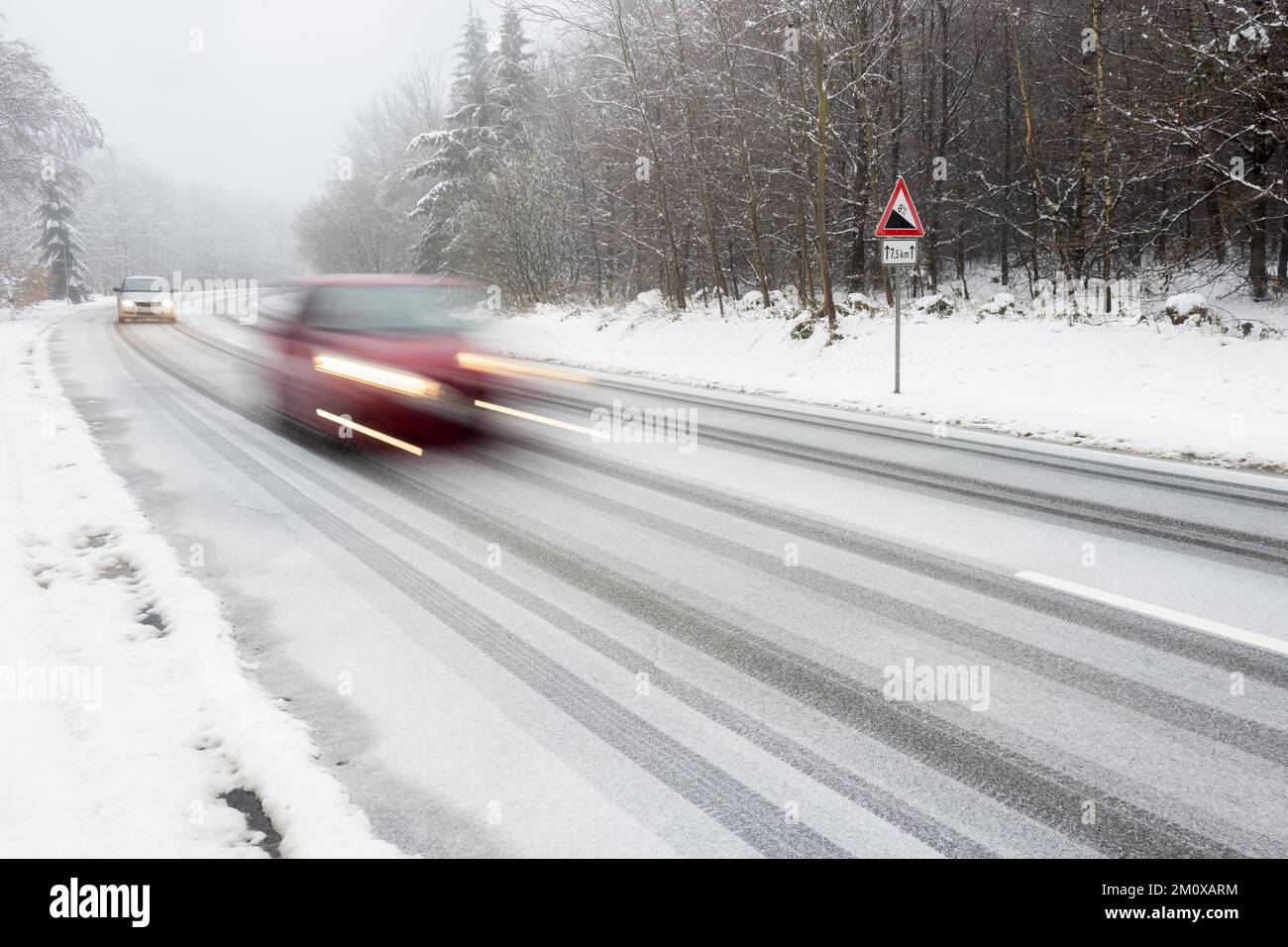 Due vetture che guidano su strade innevate, sfocatura del movimento, segnale di avvertimento in discesa, Assia, Germania, Europa Foto Stock