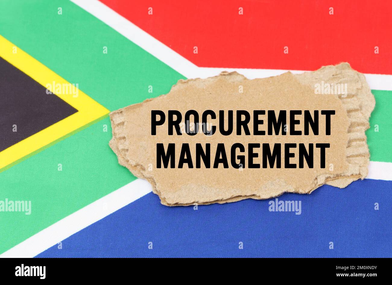 Concetto di business e finanza. Sulla bandiera del Sudafrica si trova una scatola di cartone con l'iscrizione - GESTIONE DEGLI APPALTI Foto Stock
