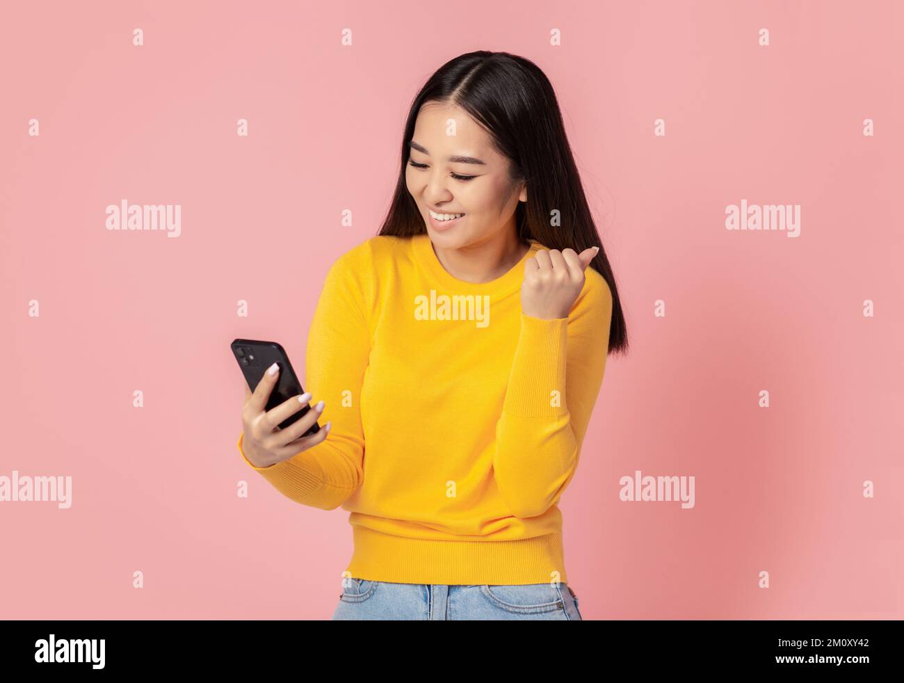 Giovane donna asiatica eccitato ha ricevuto un buon messaggio sul telefono cellulare, felice con grande notizia in piedi su sfondo rosa Foto Stock
