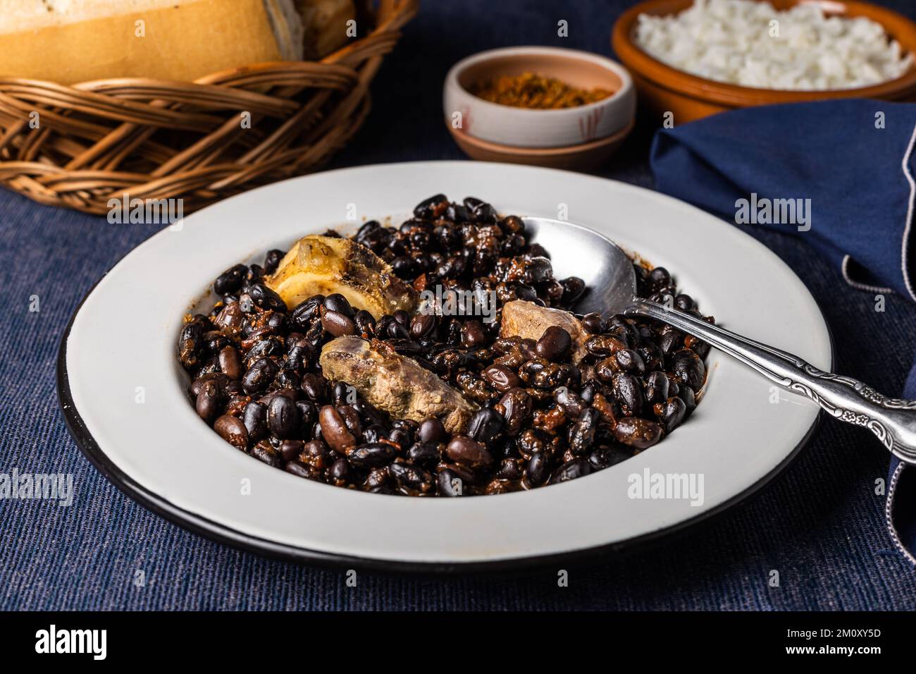 Fagioli e maiale, in piatto bianco con cucchiaio. Cibo tipico brasiliano. Foto Stock