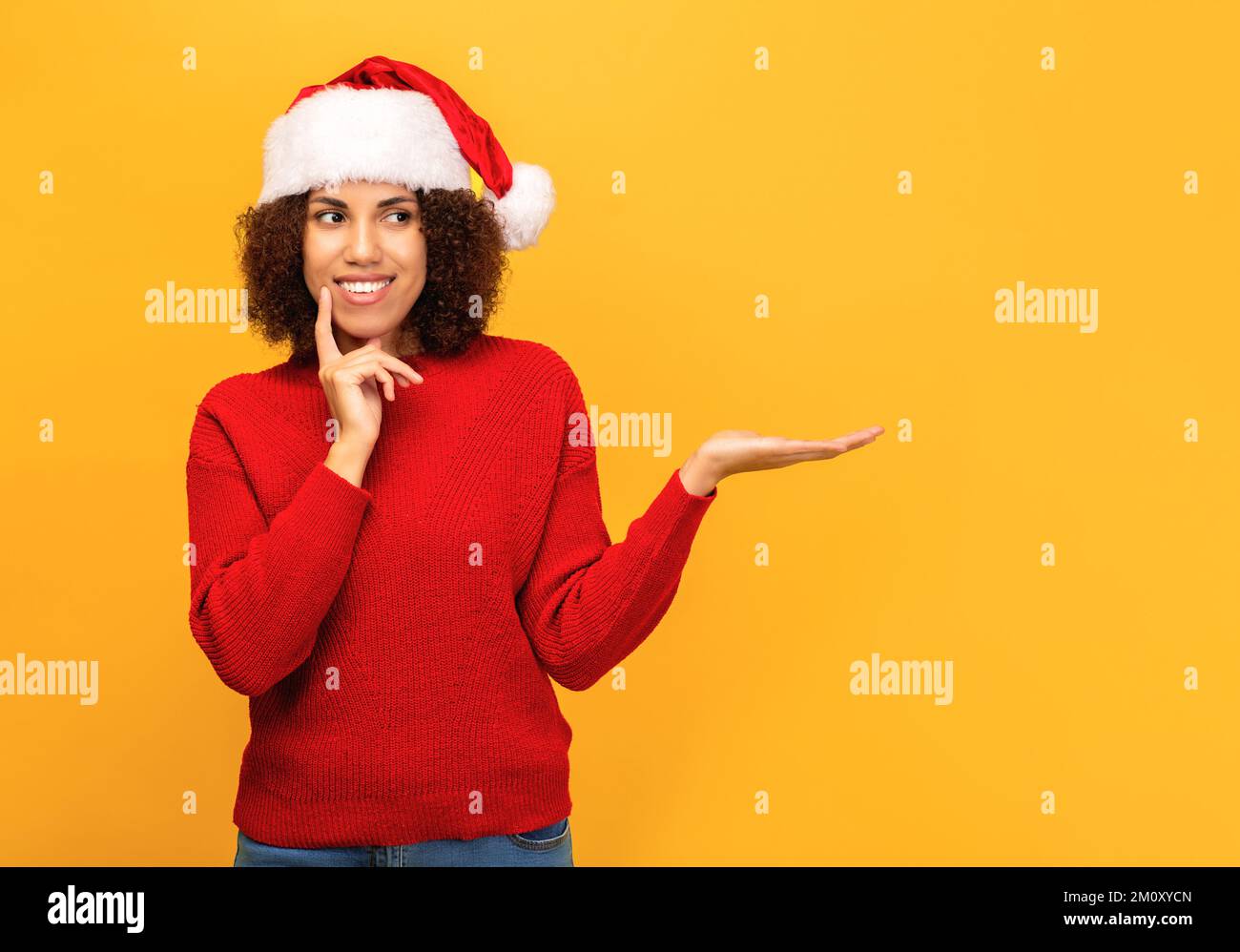 donna in un cappello di babbo natale è in piedi su sfondo arancione con una palma aperta che indica lo spazio vuoto. Natale, Natale Foto Stock
