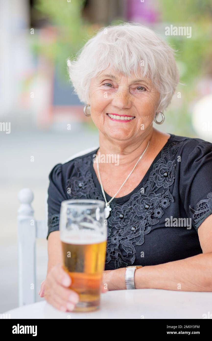 Donna matura seduta a un tavolo in un bar estivo e bere birra Foto Stock