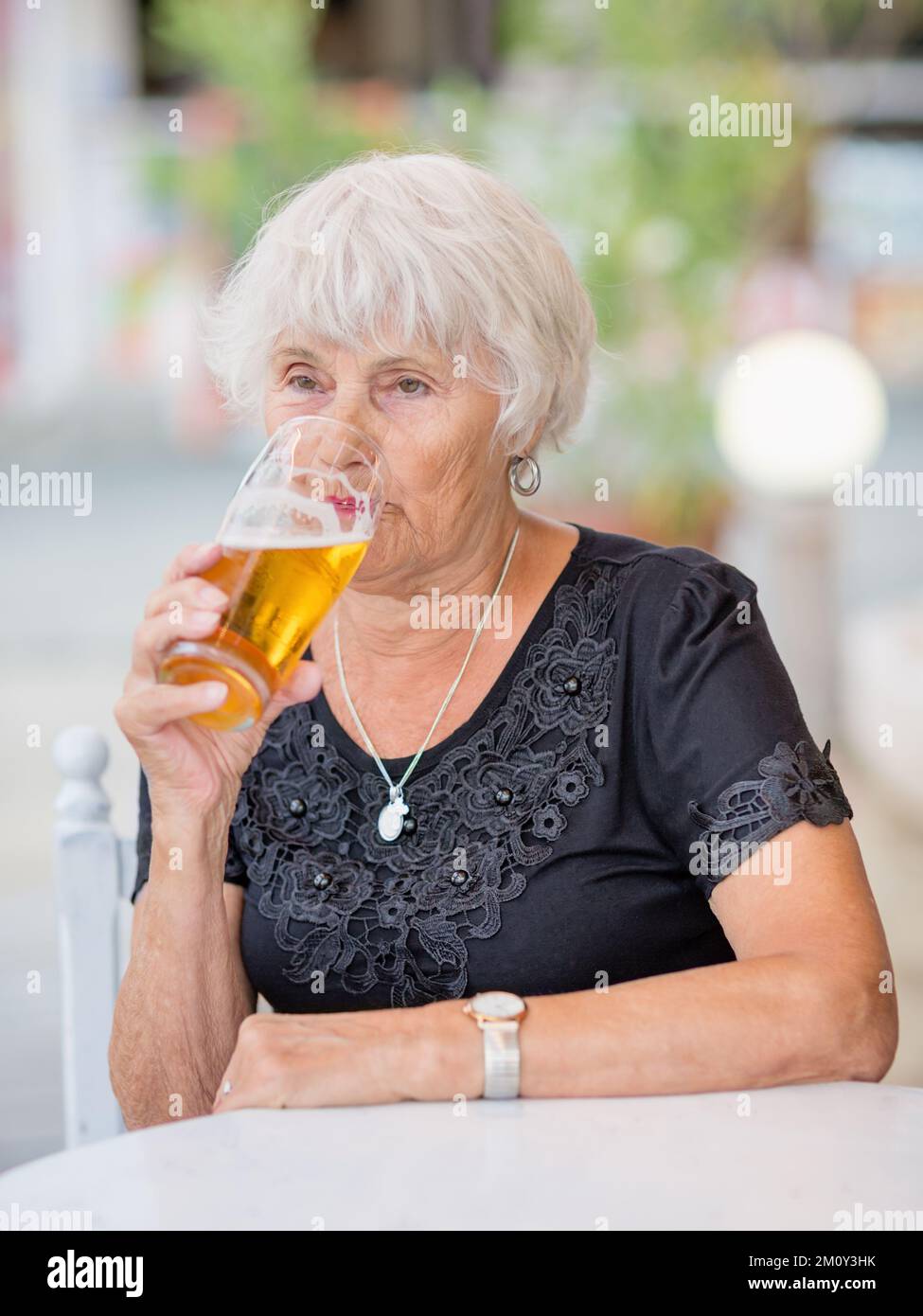 Donna matura seduta a un tavolo in un bar estivo e bere birra Foto Stock