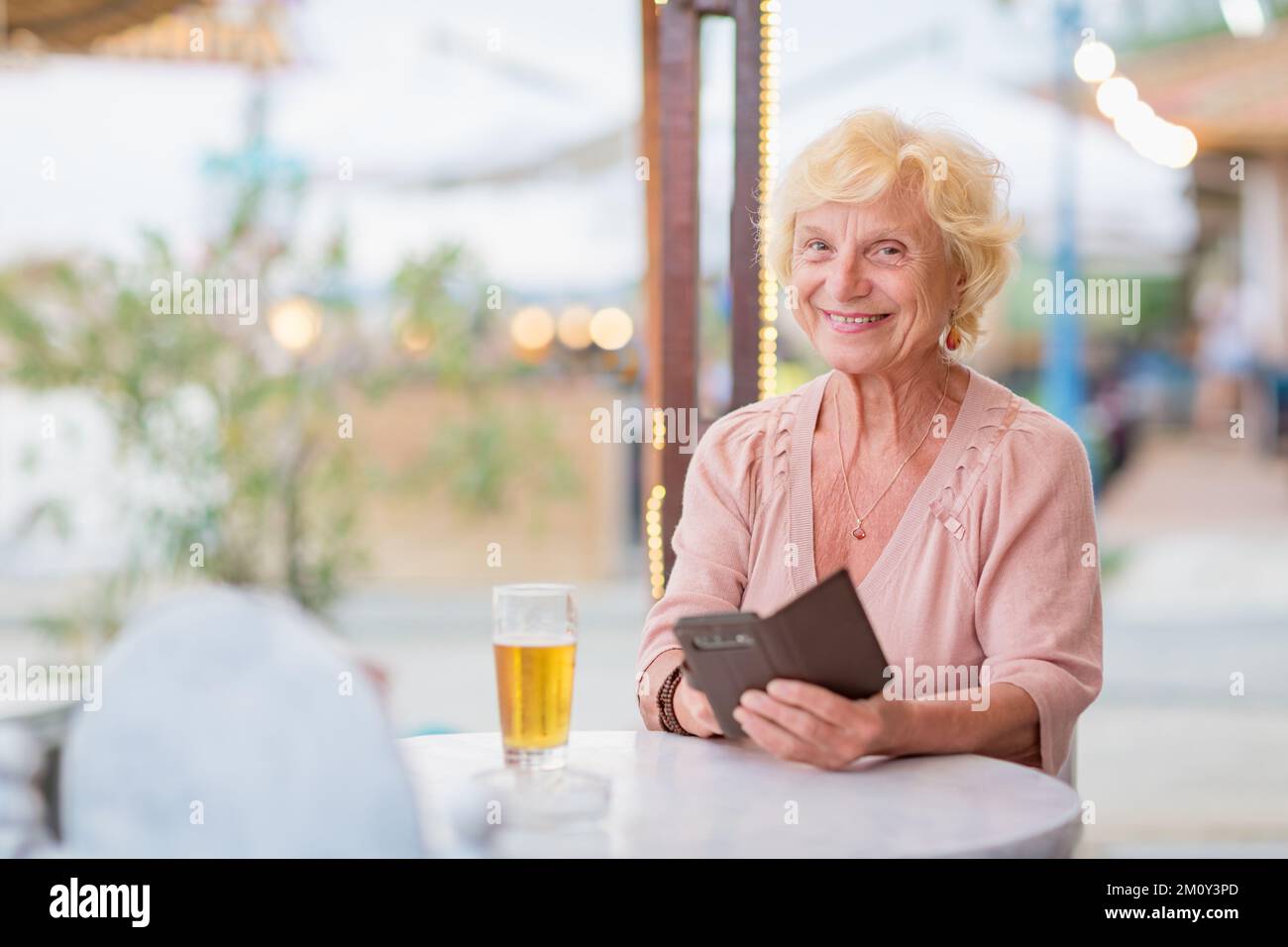 Donna matura seduta a un tavolo in un bar estivo e bere birra Foto Stock