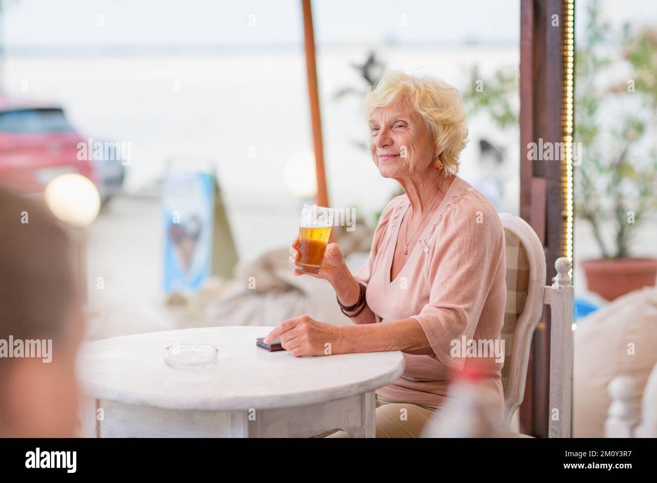 Donna matura seduta a un tavolo in un bar estivo e bere birra Foto Stock