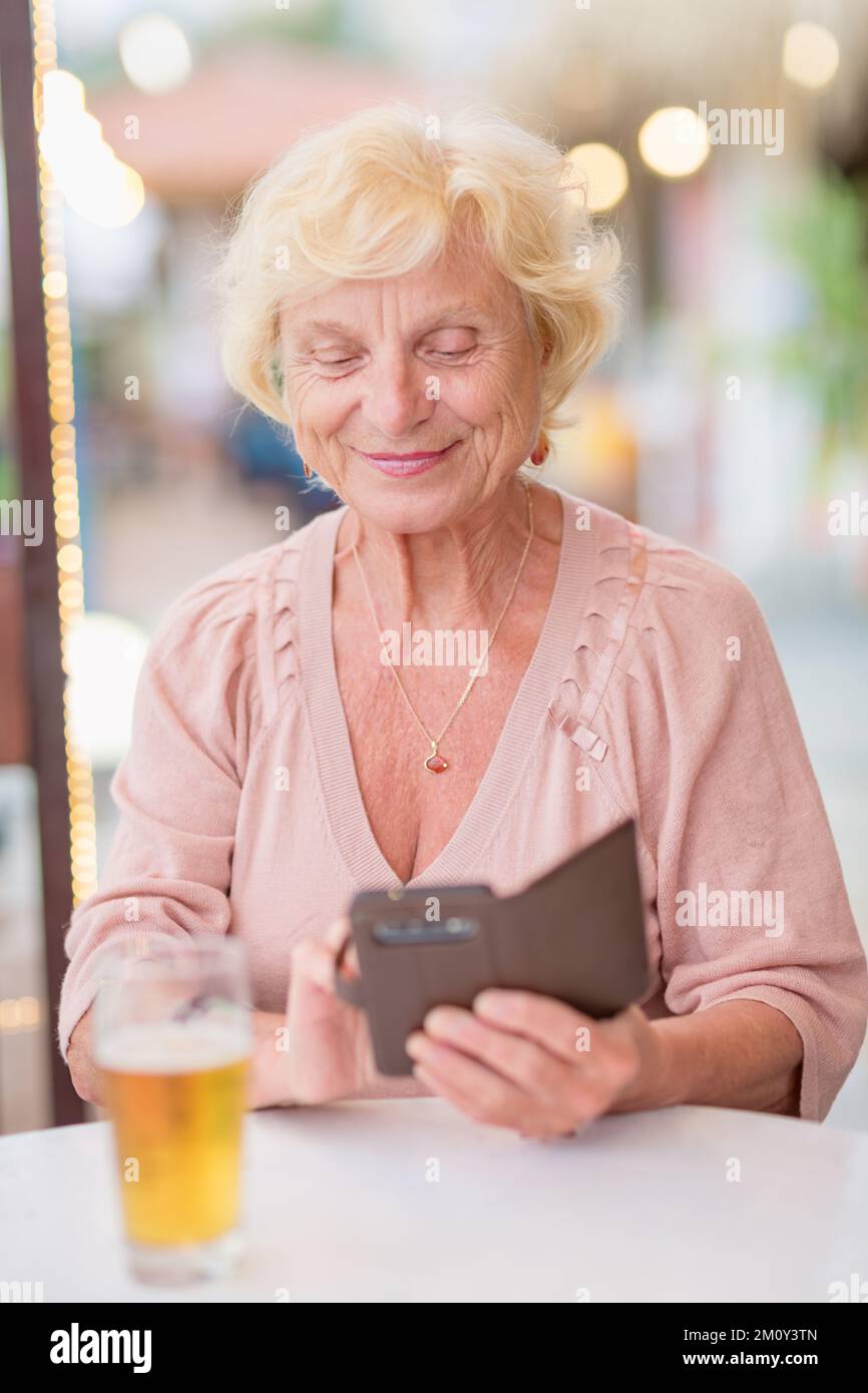 Donna matura seduta a un tavolo in un bar estivo e bere birra Foto Stock