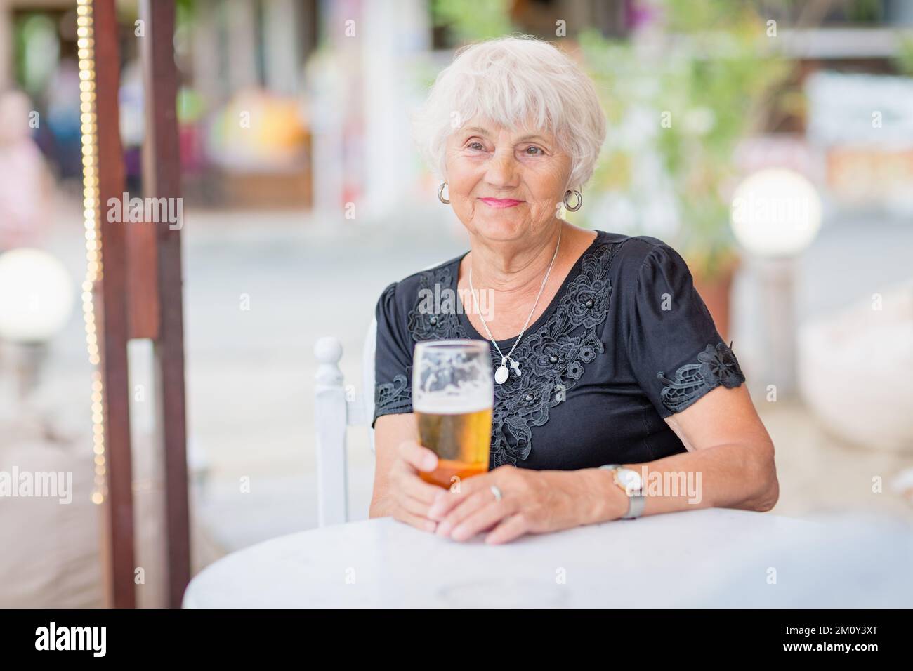 Donna matura seduta a un tavolo in un bar estivo e bere birra Foto Stock