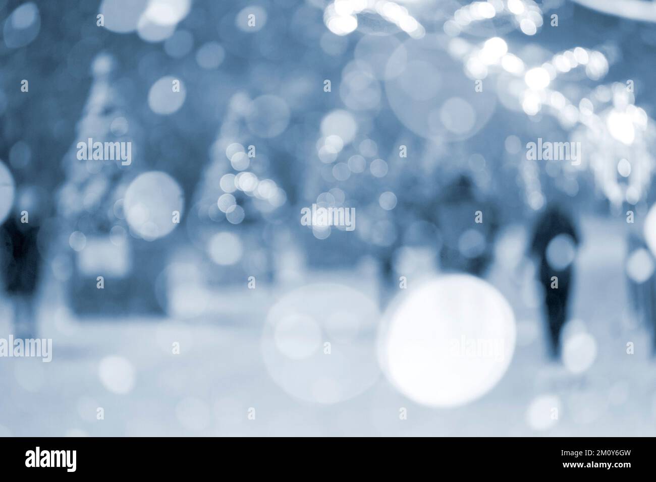 Sfondo sfocato astratto. Persone che camminano per strada di alberi di Natale decorati illuminazione luminosa decorata, luci e ghirlande in città durante la forte nevicata nella notte d'inverno colore blu Foto Stock