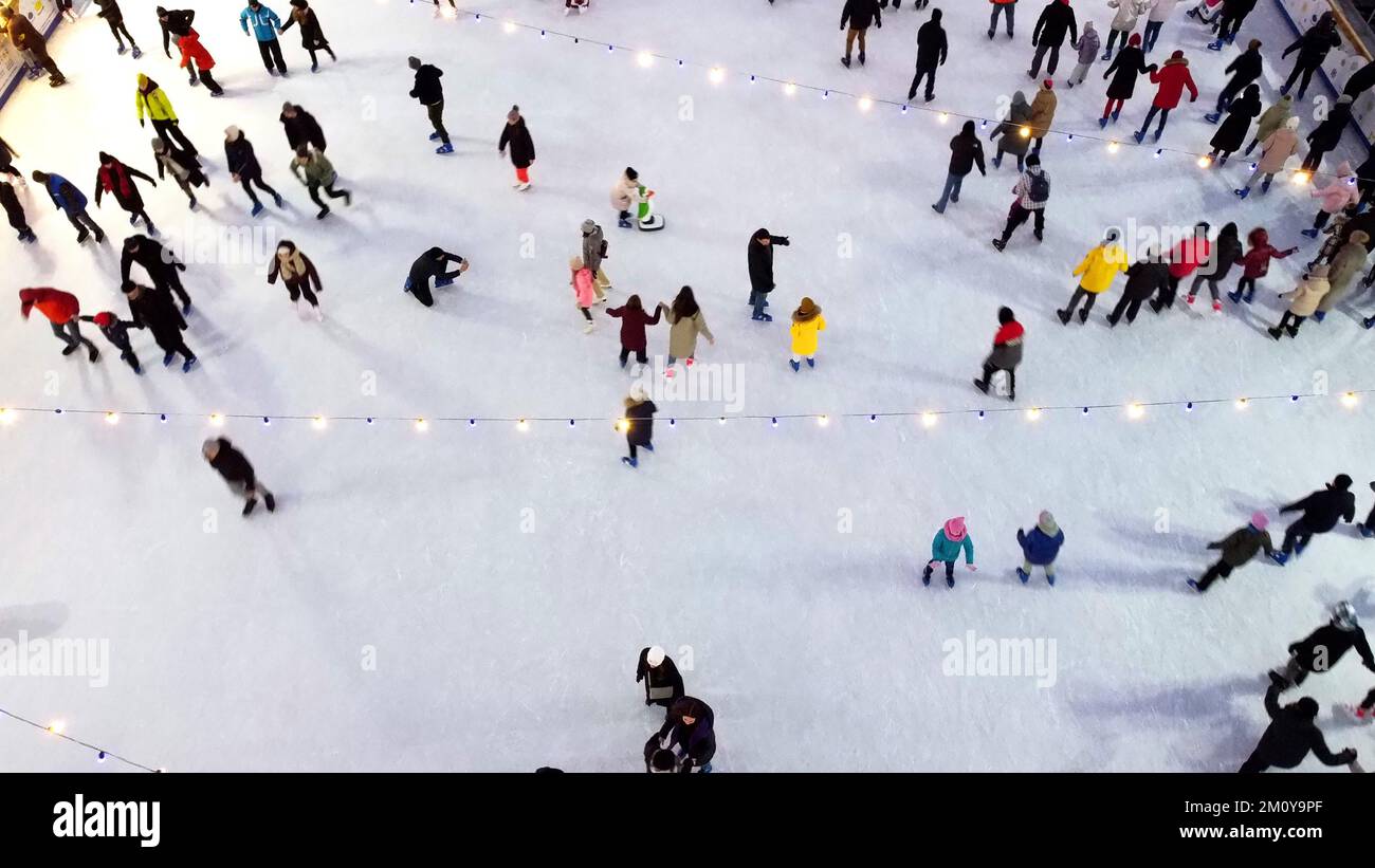 Vista aerea molte persone pattinano su una pista di pattinaggio all'aperto in inverno. Vista dall'alto sul pattinaggio su ghiaccio. Pista di pattinaggio sul ghiaccio del parco cittadino. Attività invernali all'aperto. Pattinaggio vacanze sfondo. Luci di Natale di Capodanno Foto Stock