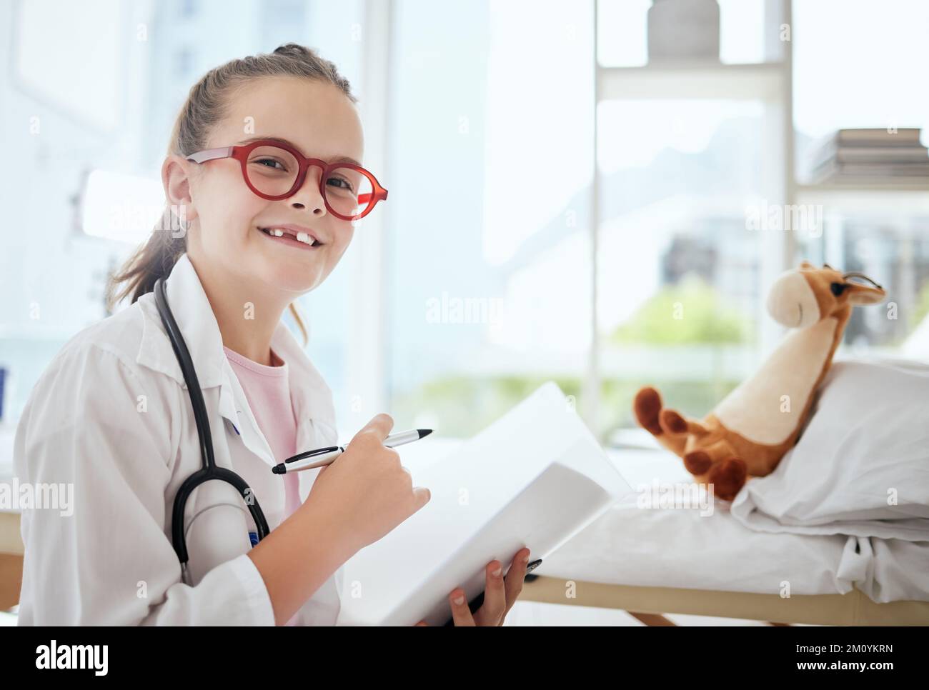 Immaginate di essere chi sognate di essere. una bambina che finge di essere un medico mentre esamina il suo animale farcito a casa. Foto Stock