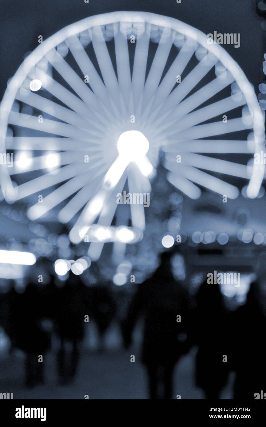 Illuminazione decorata ruota panoramica, albero di Natale, silhouette nere di persone che camminano, edifici cittadini nella notte d'inverno. Città di Natale. Capodanno Natale vacanza sfondo sfocato colore blu Foto Stock