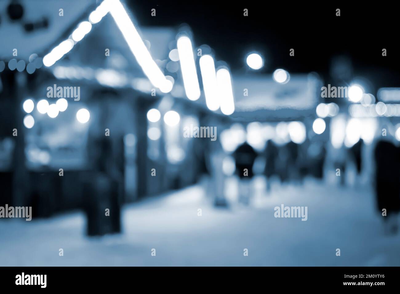 Sfondo sfocato. Persone che camminano in piazza la notte d'inverno. Silhouette persone che camminano vicino a case decorate illuminazione luminosa. Luce bianca spot bokeh da luci di casa incandescente colore blu Foto Stock