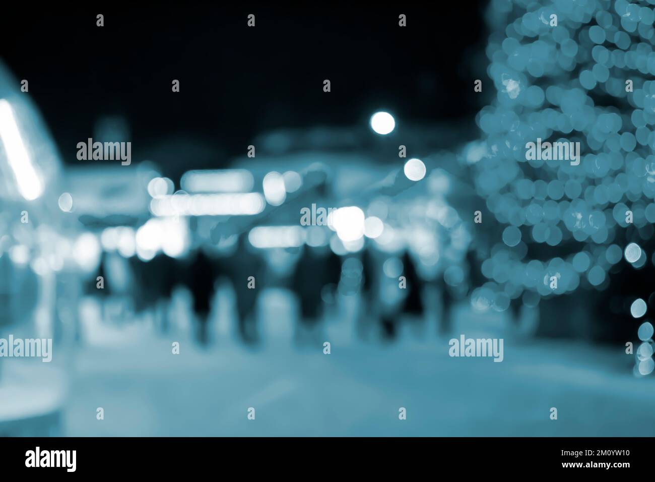 Sfondo sfocato. Albero di Natale, luci luminose decorate, silhouette di costruzione di persone che camminano la piazza della città durante la notte d'inverno. Bello Capodanno e Natale vacanza sfondo sfocato colore blu Foto Stock