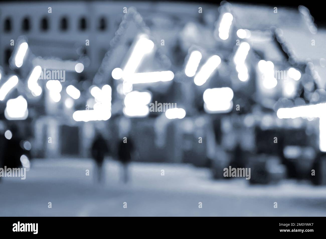 Sfondo sfocato. La gente cammina in città la notte d'inverno. Silhouette nere di persone che camminano vicino a case decorate illuminazione luminosa. Luce bianca spot bokeh da luci di casa incandescente colore blu Foto Stock