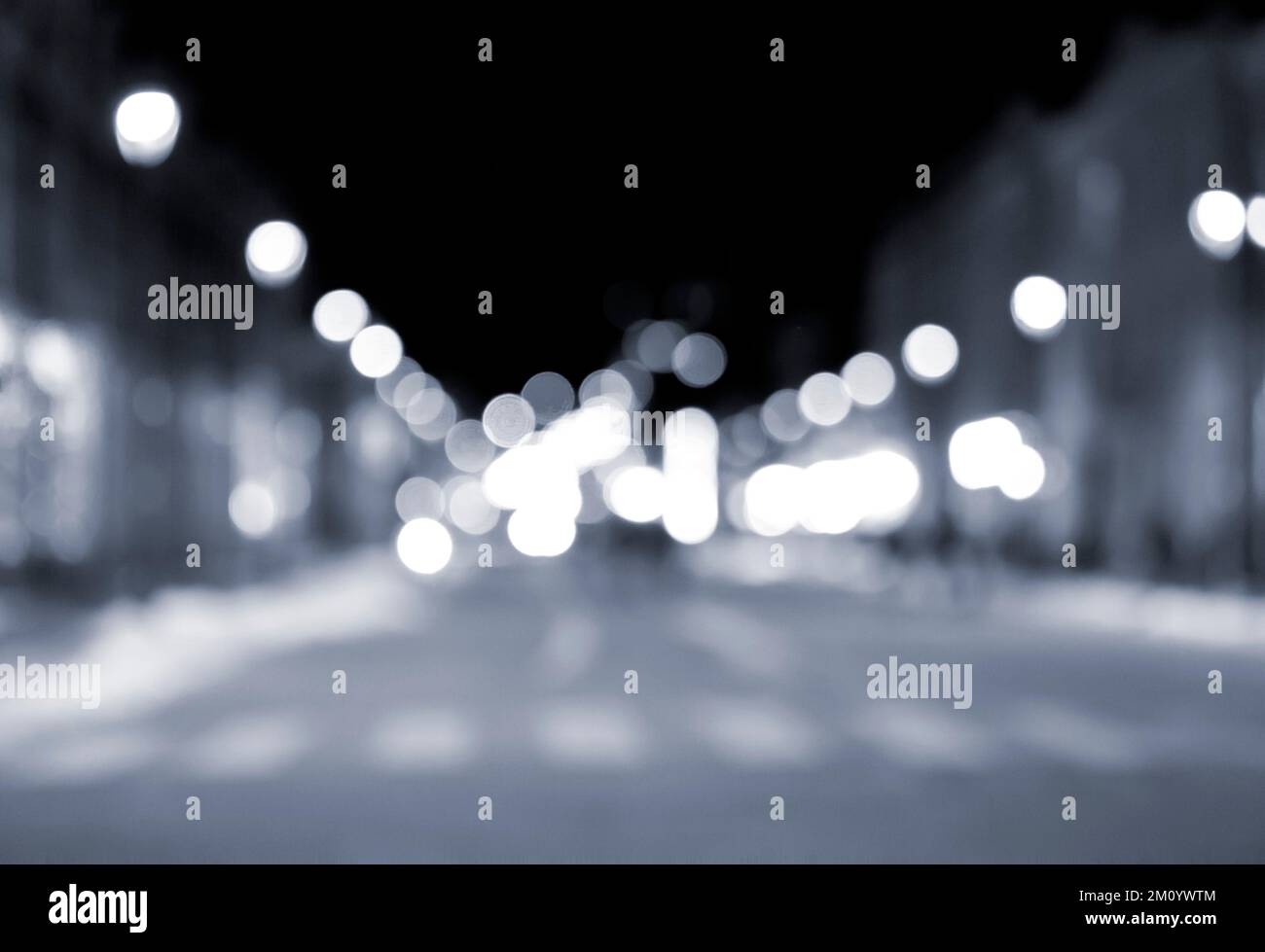 Sfondo sfocato. Notte città. Silhouette sfocata degli edifici, macchie bokeh di lanterne luminose, silhouette sfocate di persone che camminano per strada di sera. Piazza della città, cielo notturno nero di colore blu Foto Stock