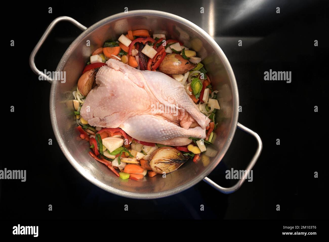 Ingredienti per una zuppa sana con un pollo intero e verdure in una pentola di acciaio inossidabile sulla stufa nera, cottura per il sistema immunitario contro Foto Stock