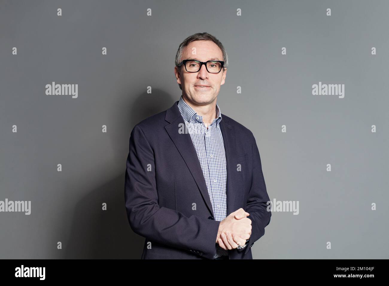 Uomo d'affari maturo in tuta blu, camicia e occhiali a quadri blu e bianchi si trova su sfondo grigio Foto Stock