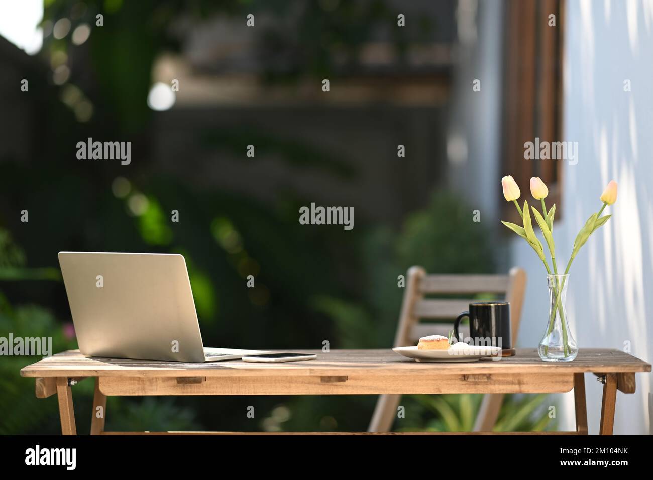 Computer portatile, tazza di caffè, notebook e vaso da fiori su un tavolo di legno all'aperto Foto Stock