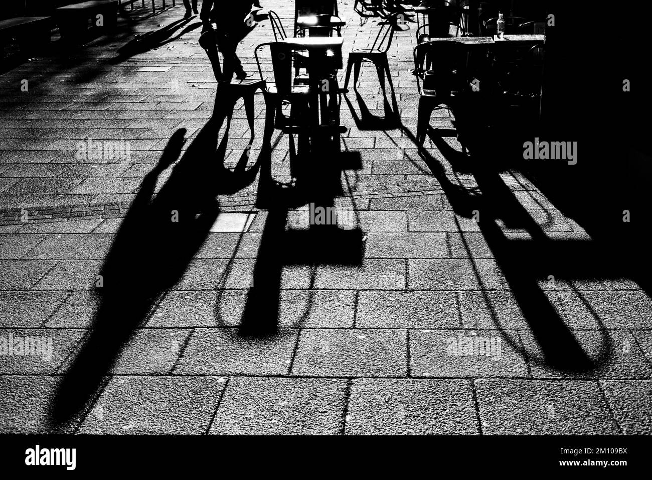 Lunghe ombre di sedie, tavoli e figure in bianco e nero. Retroilluminazione spettacolare con ombre che arrivano direttamente verso la fotocamera.concetto di ombra Foto Stock