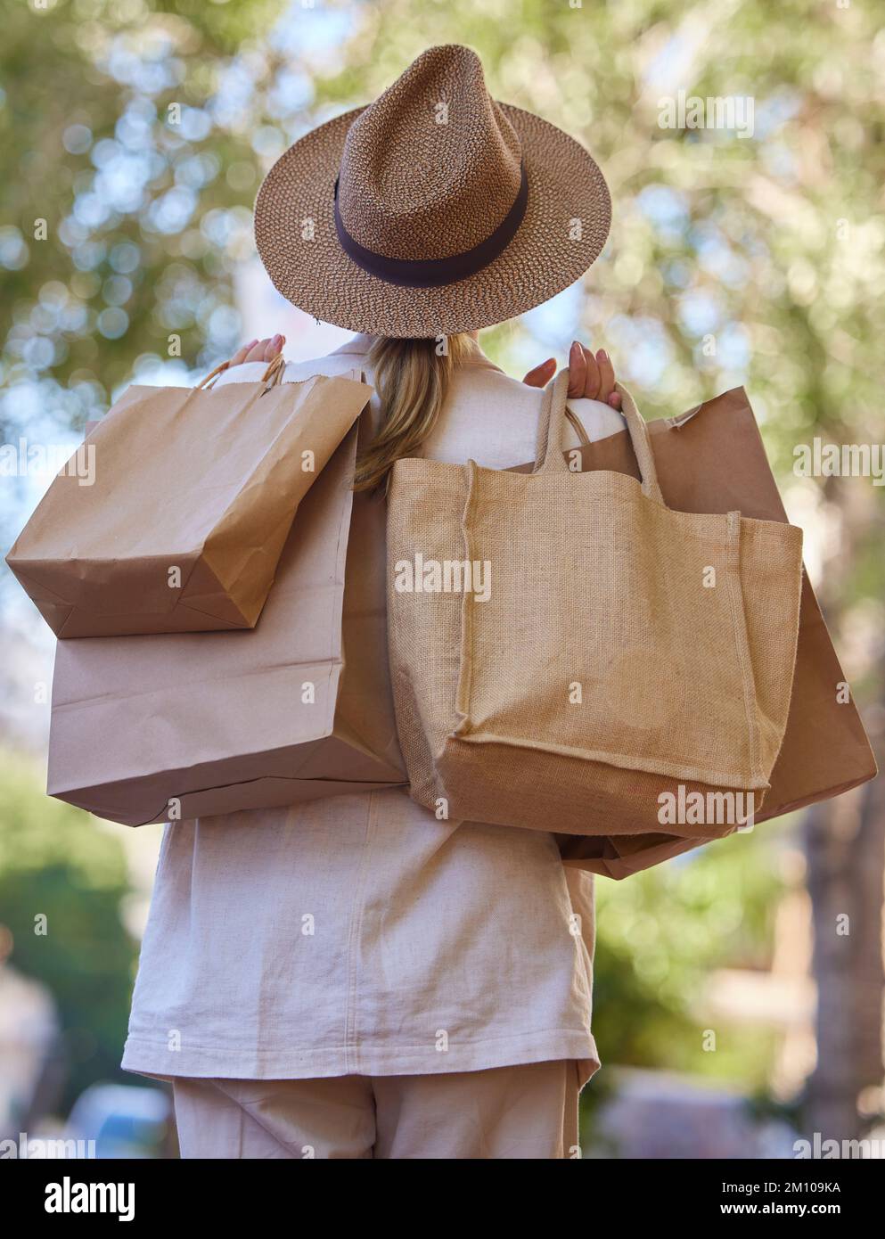 Sole, alberi e donna con borse dallo shopping dalla parte posteriore a piedi nel parco in vacanza. Estate, natura e viaggi, ragazza con shopping bag di lusso Foto Stock