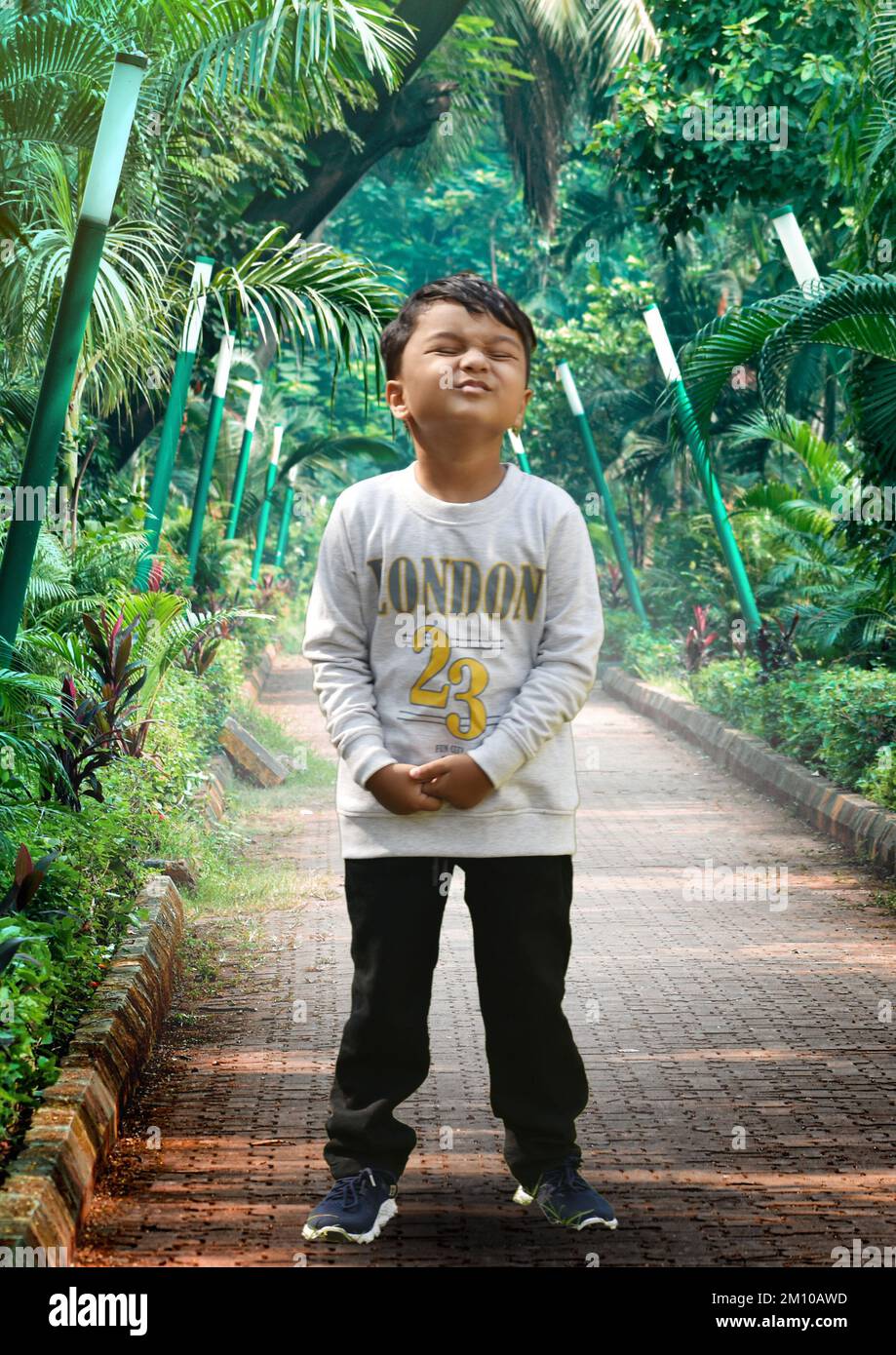 Un ragazzino che gioca in giardino, un giovane ragazzino indiano che gioca a calcio nel giardino del parco all'aperto guardando la macchina fotografica. Calcio maschile sorridente sportivo asiatico Foto Stock