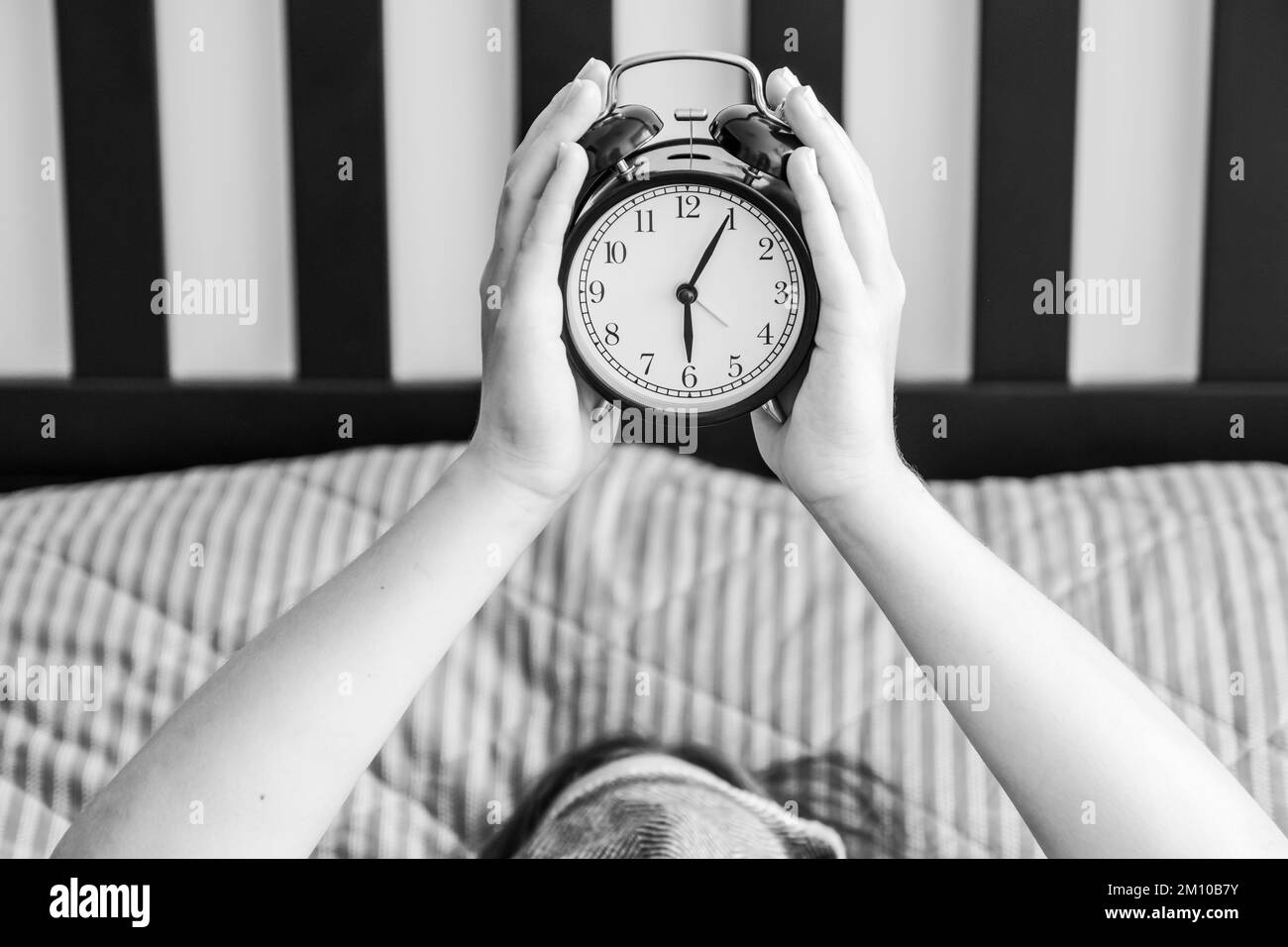 Persona sdraiata a letto con una sveglia nelle mani alle sei del mattino Foto Stock