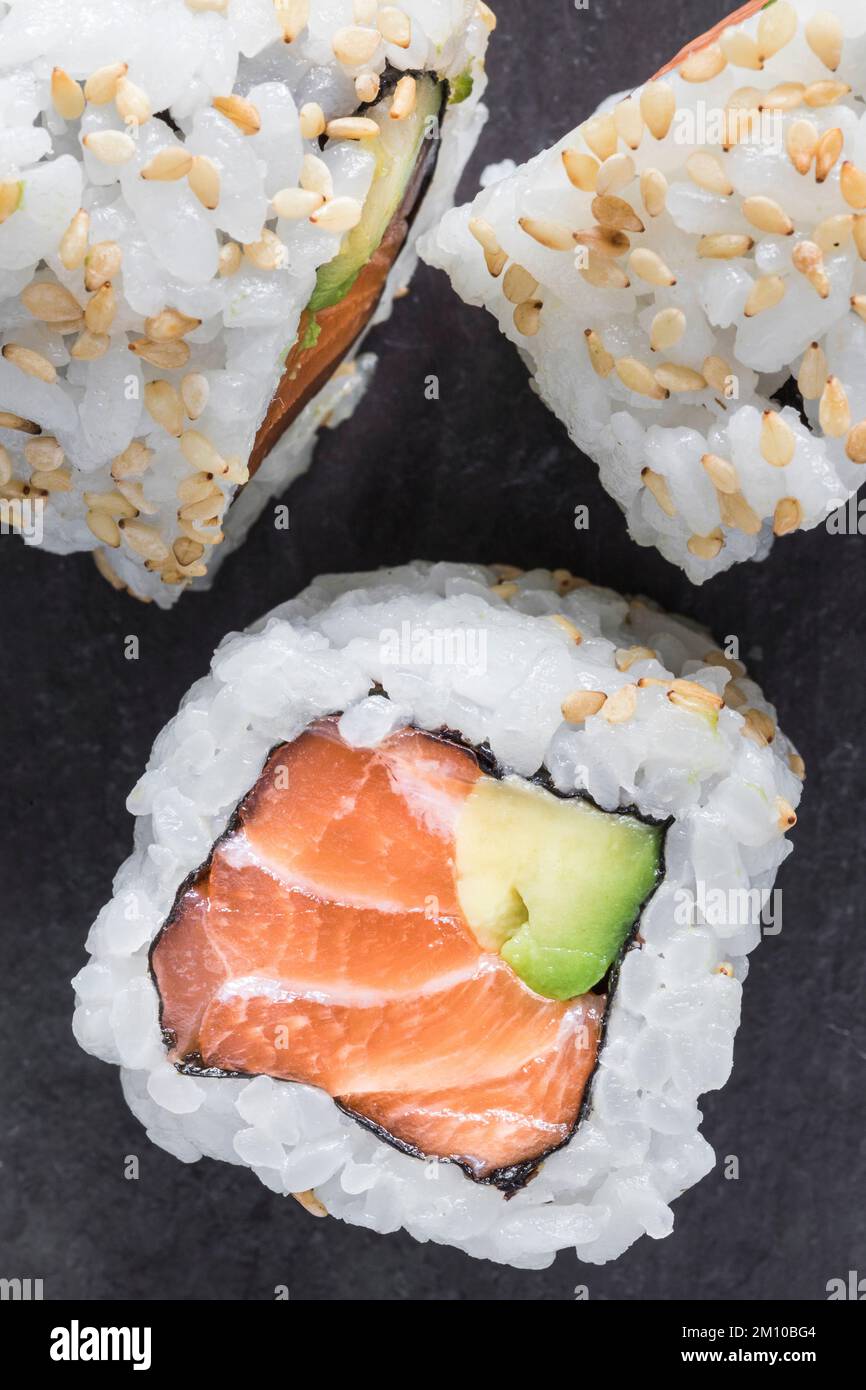 Uramaki di salmone e avocado con semi di sesamo su fondo nero. Vista dall'alto. Scatto macro Foto Stock