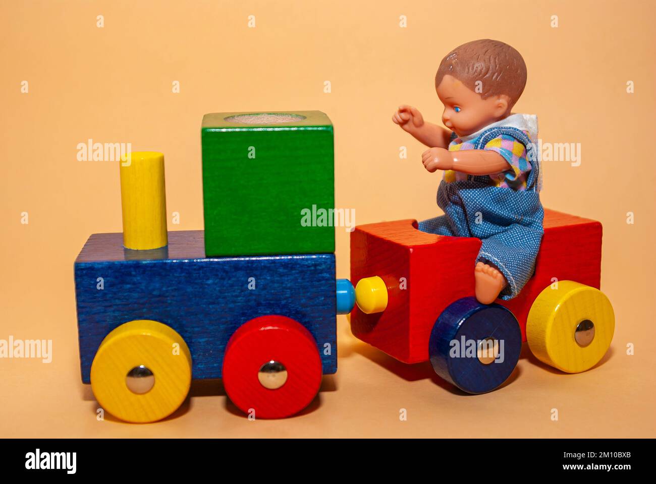 Una bambola bambino siede su un trenino giocattolo fatto di legno, anche concetto di gioco infantile e di viaggio in treno. Foto Stock