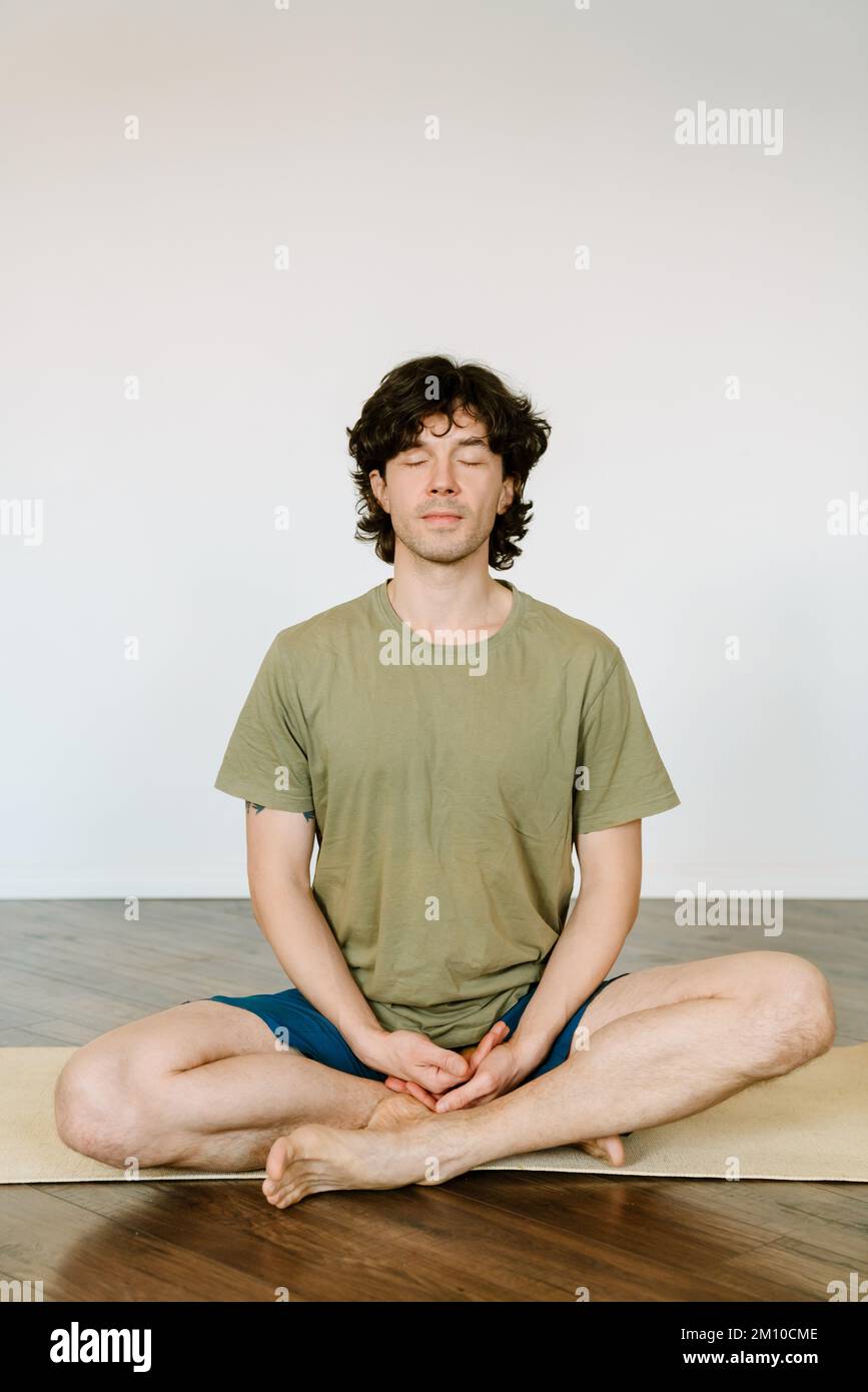 Uomo bianco che indossa pantaloncini che meditano durante lo yoga a casa Foto Stock