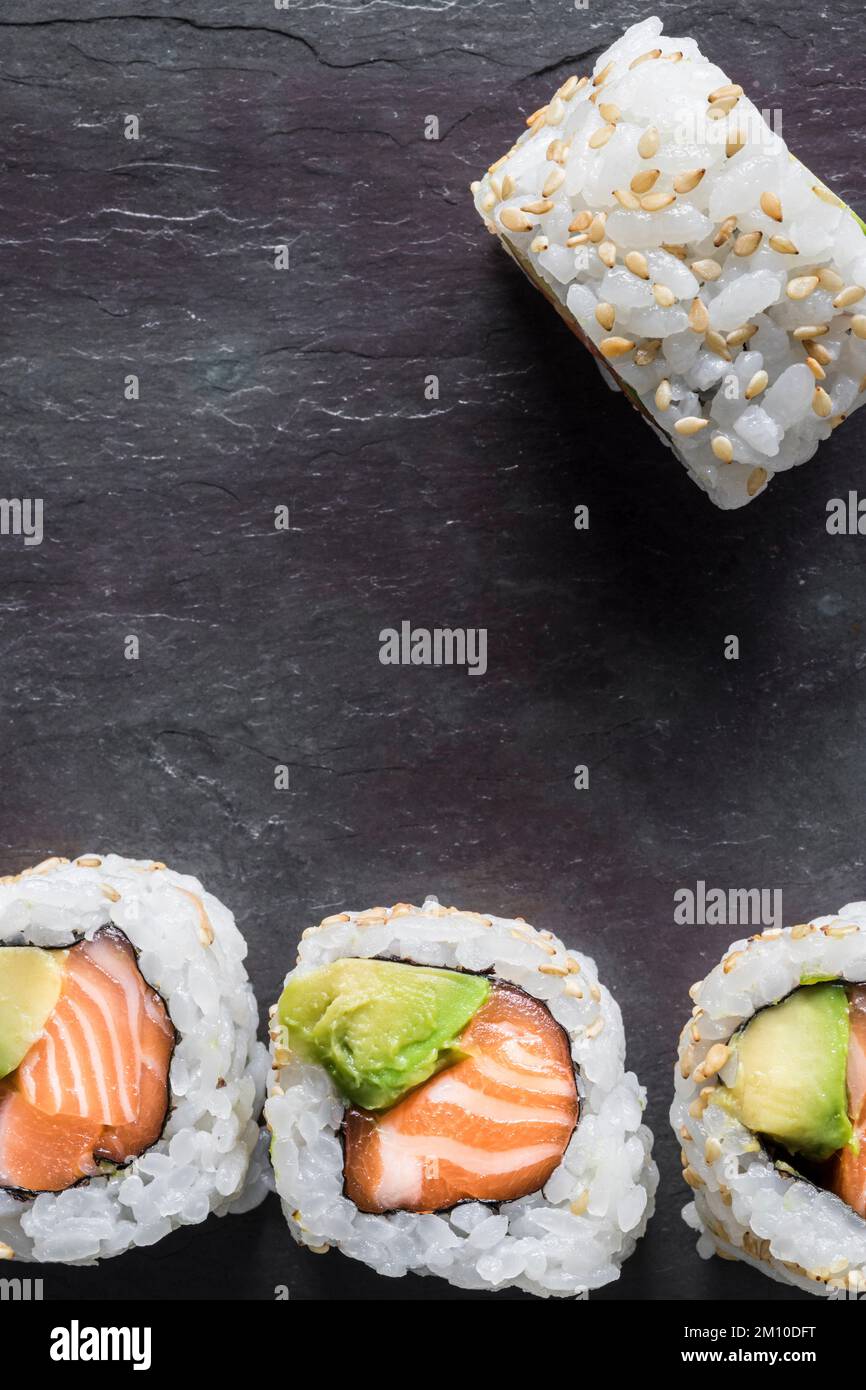 Uramakis di salmone e avocado con semi di sesamo su fondo nero. Vista dall'alto. Scatto macro. Spazio di copia. Foto Stock