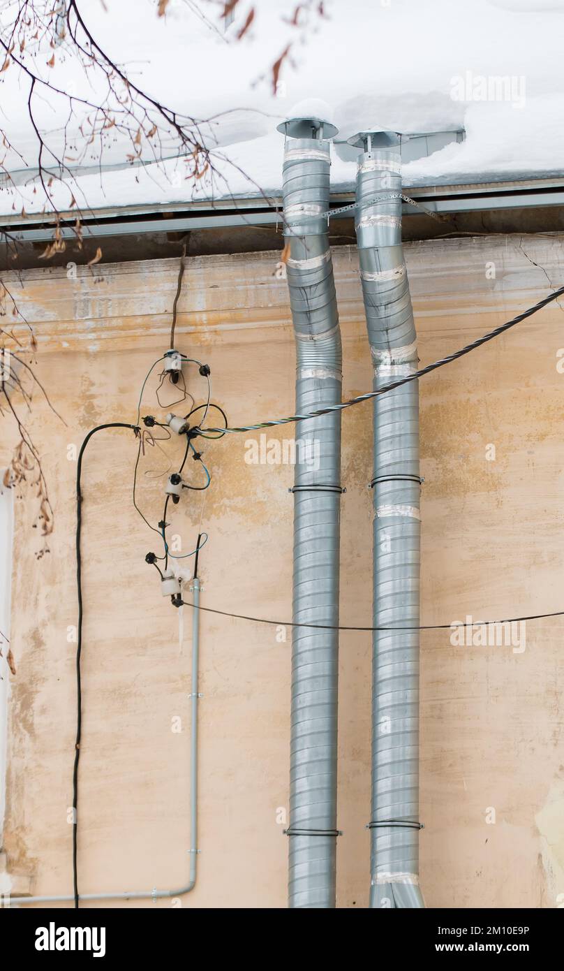 Due tubi di ventilazione di scarico in metallo sullo sfondo della parete della casa. Il tetto dell'edificio in neve bianca. Nuvoloso, freddo giorno d'inverno, luce soffusa. Foto Stock