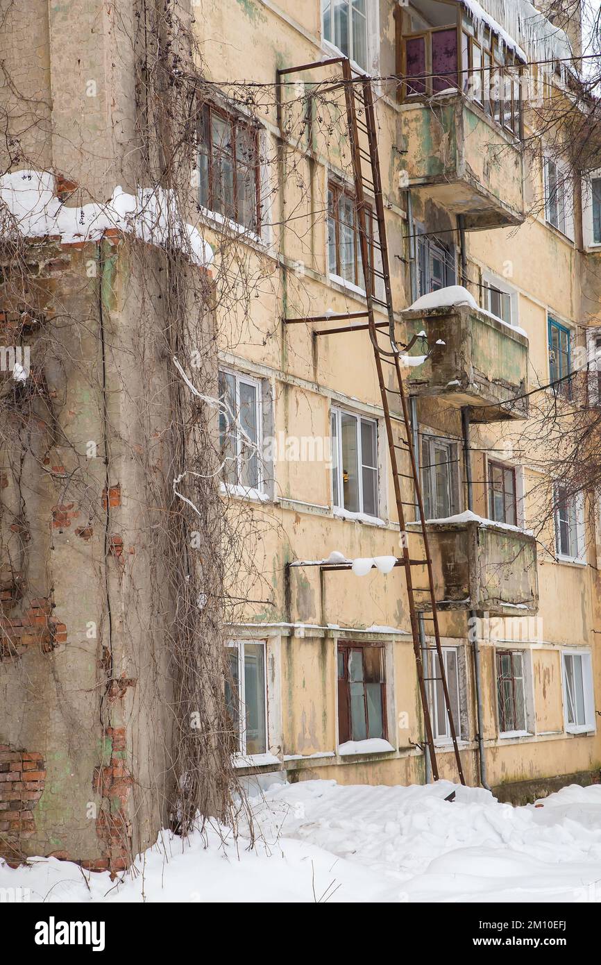 Una piccola nevicata sullo sfondo del muro di un edificio residenziale. Sulla strada si trova la neve bianca in alto mucchi. Paesaggio urbano invernale. Nuvoloso giorno d'inverno, luce soffusa. Foto Stock