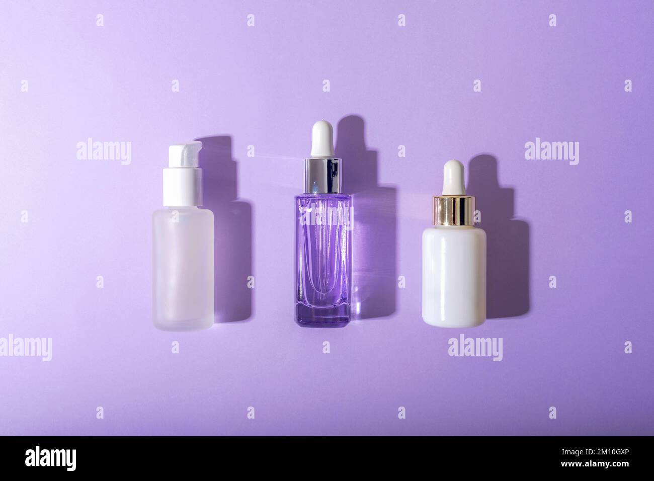 Flaconi di siero cosmetico su sfondo viola con ombre dure. Vista dall'alto, piatto, mockup. Foto Stock