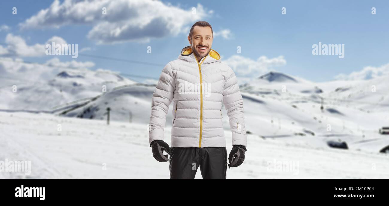 Giovane sorridente con una giacca invernale che si posa su una montagna innevata Foto Stock