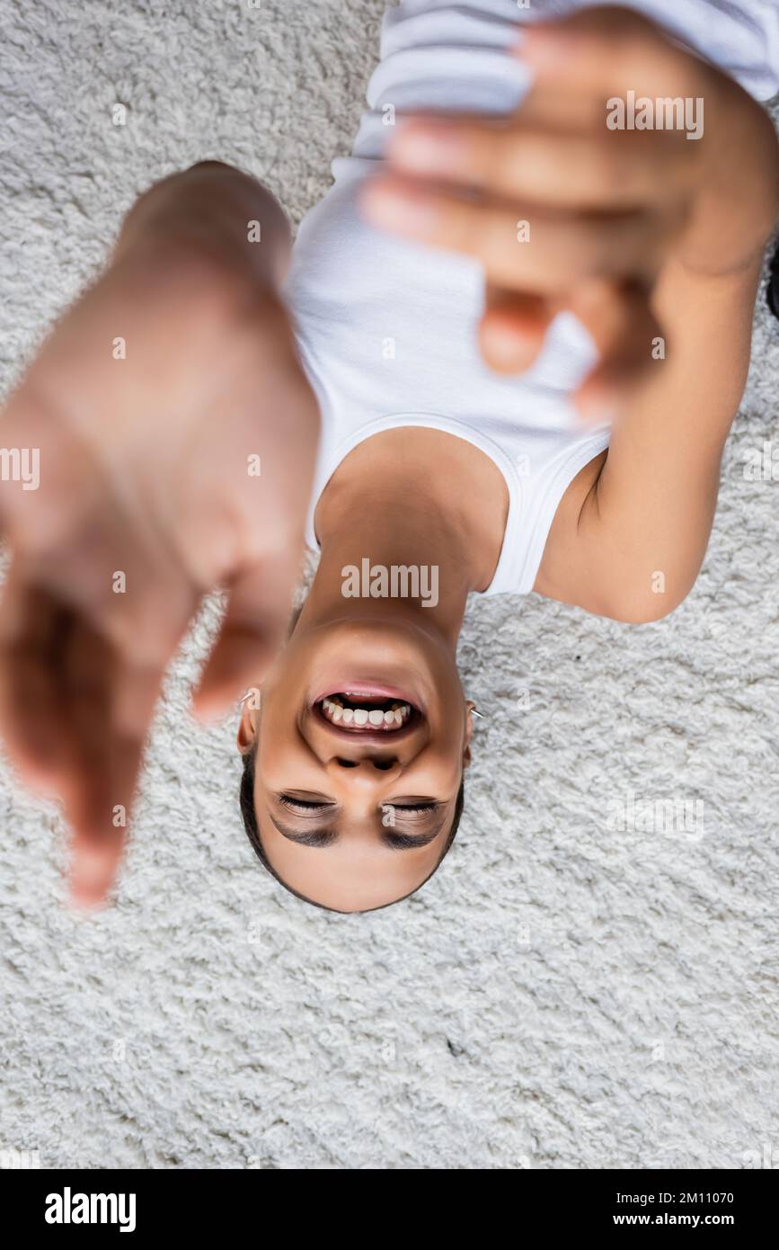 vista dall'alto di una donna afro-americana positiva in canotta sdraiata sul tappeto, immagine stock Foto Stock