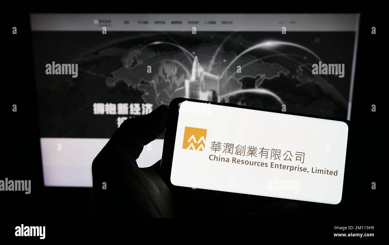 Persona che detiene uno smartphone con il logo della società China Resources Enterprise Limited sullo schermo davanti al sito Web. Messa a fuoco sul display del telefono. Foto Stock