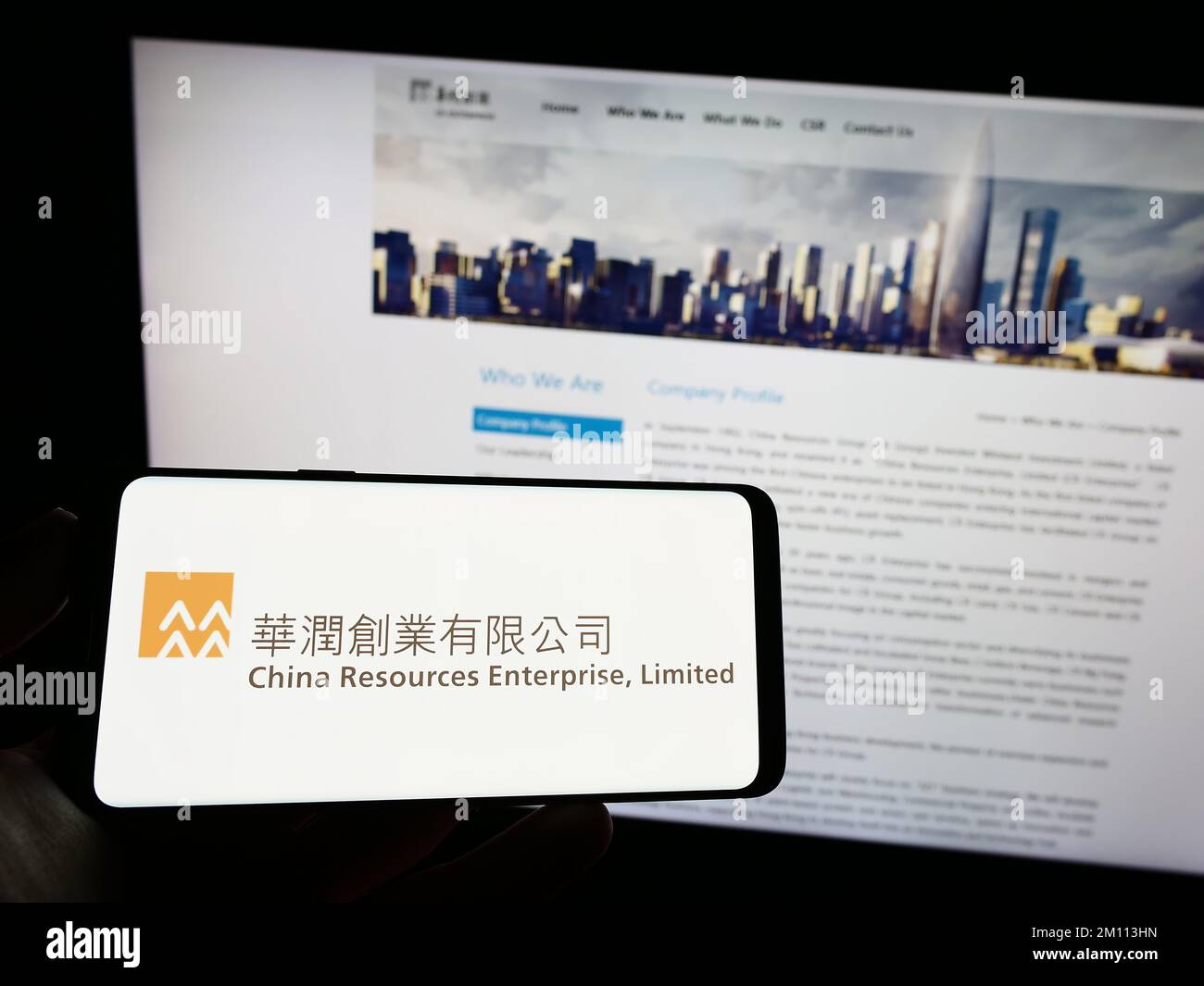 Persona che tiene il cellulare con il logo della società China Resources Enterprise Limited sullo schermo di fronte alla pagina Web aziendale. Messa a fuoco sul display del telefono. Foto Stock