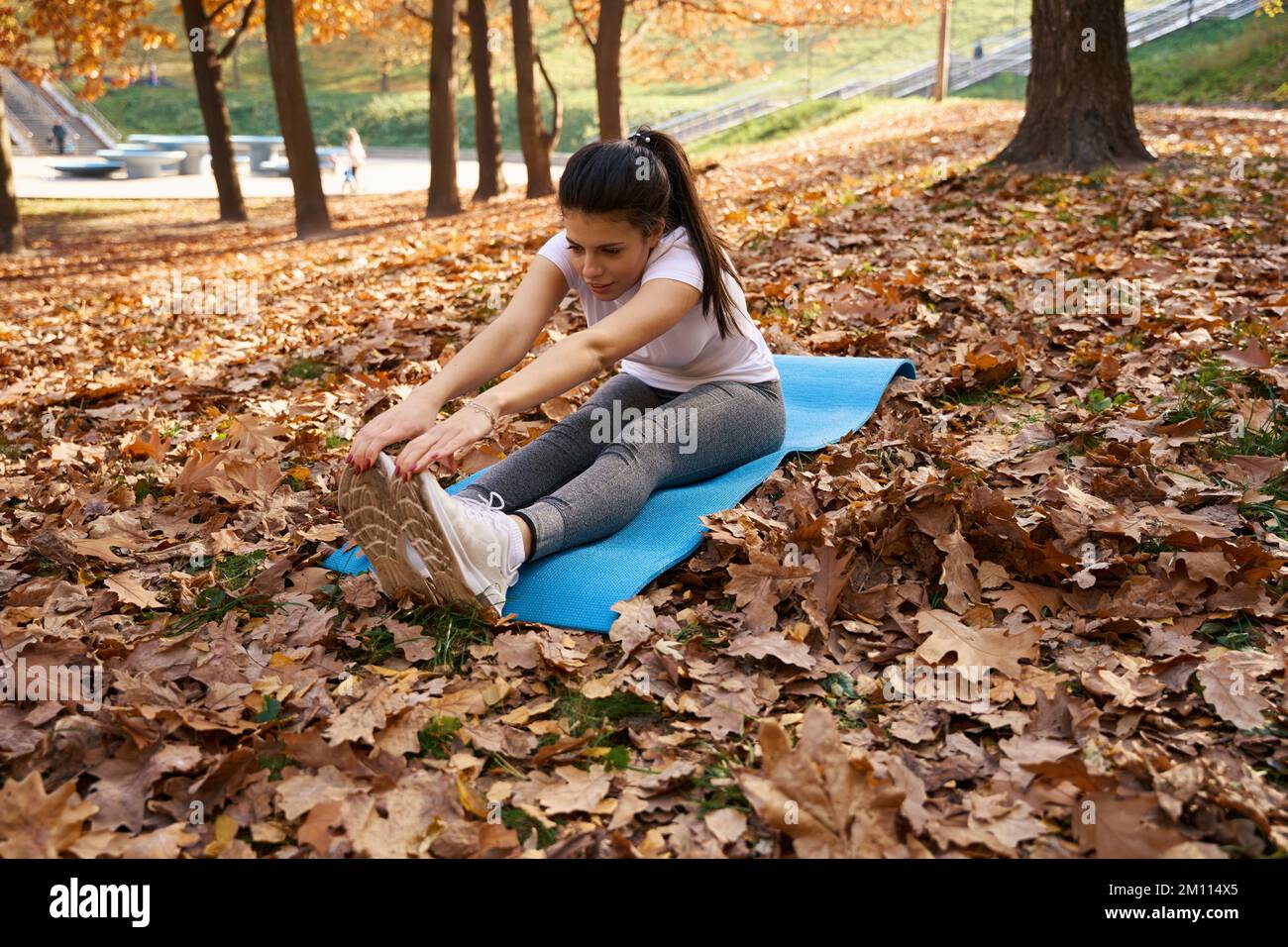 Donna che si estende su un carimate blu in un parco cittadino Foto Stock