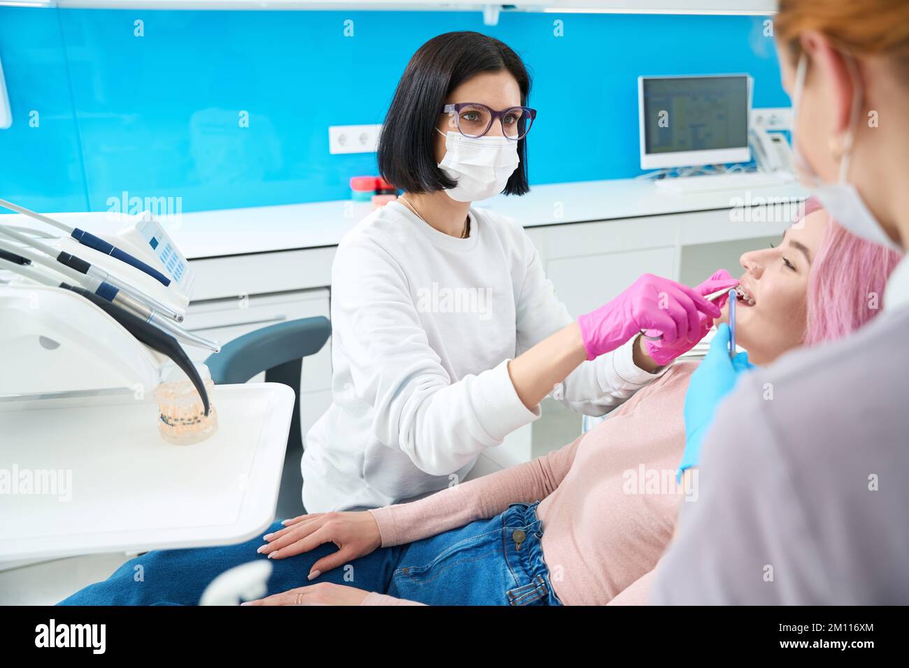 Ortodontista con assistente eseguire la manutenzione del sistema di rinforzi sul paziente Foto Stock