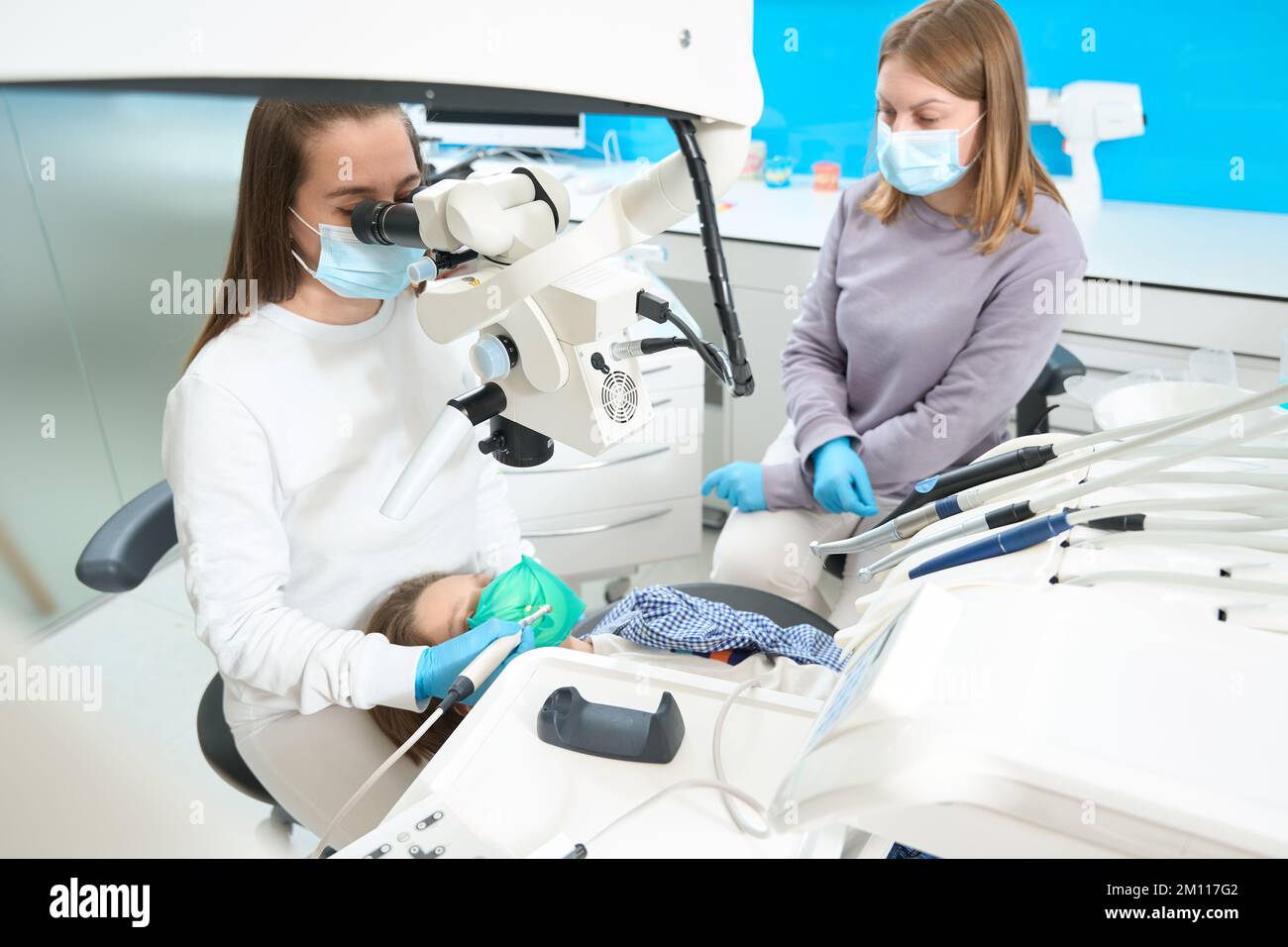 Il dentista sta trattando il dente del ragazzo sotto il microscopio, usa l'apparecchiatura moderna Foto Stock
