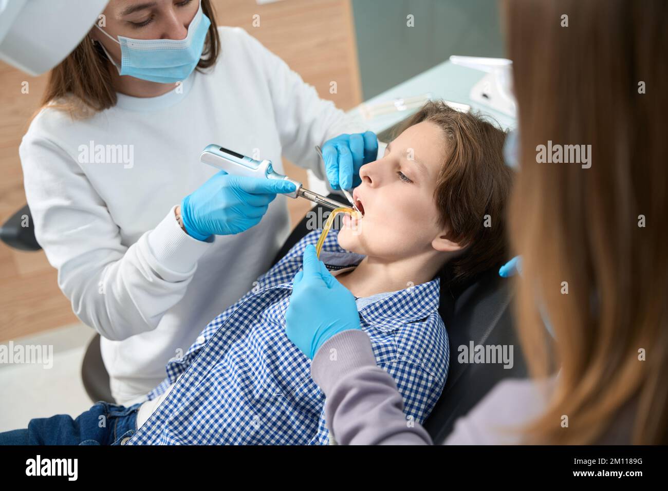 Donna dentista sul posto di lavoro tratta dente di un ragazzo Foto Stock