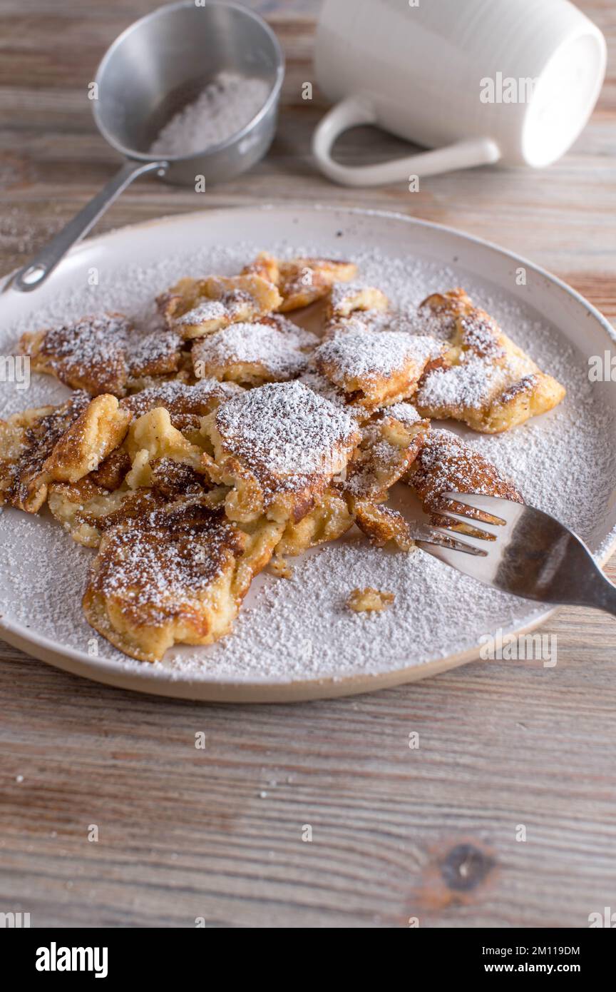 kaiserschmarrn fatto in casa con zucchero a velo su un piatto bianco su sfondo di legno chiaro Foto Stock