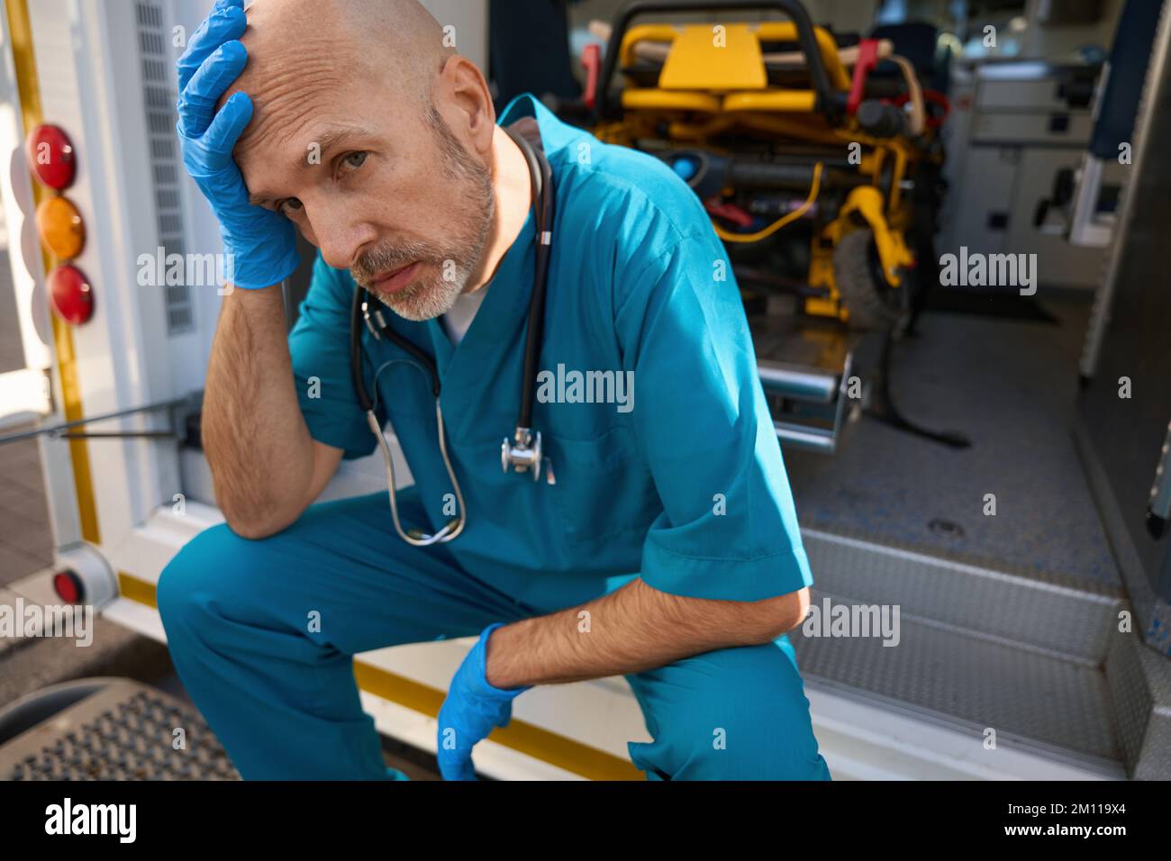 L'uomo in uniforme medica siede sul bordo di un'ambulanza Foto Stock