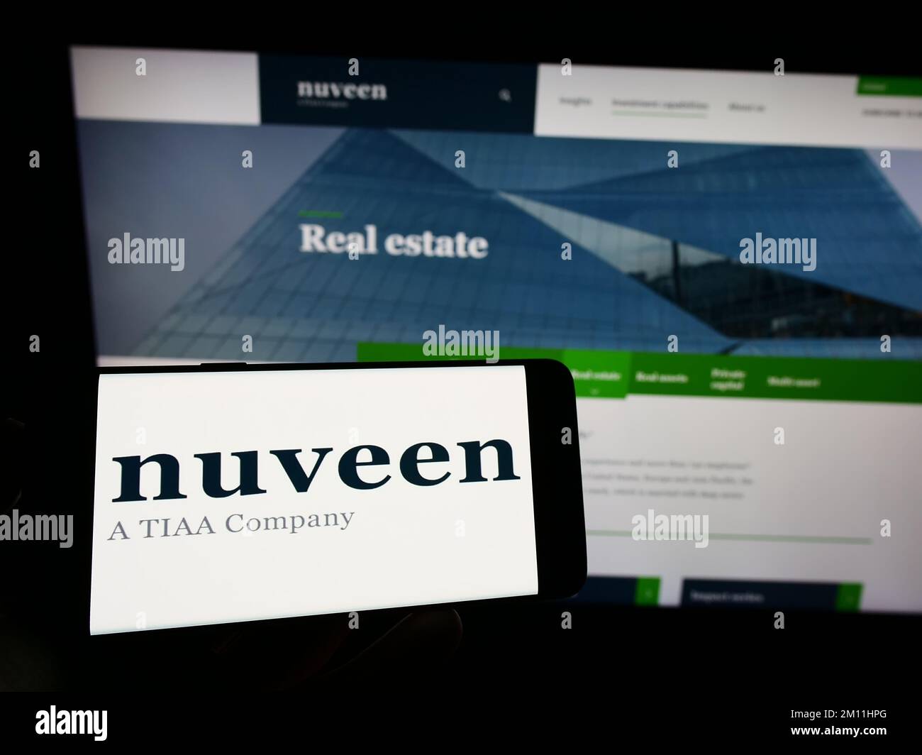 Persona che tiene il telefono cellulare con il logo della società americana di gestione patrimoniale Nuveen sullo schermo di fronte alla pagina web aziendale. Messa a fuoco sul display del telefono. Foto Stock